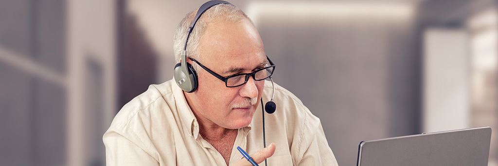 A man sitting at a laptop with a headset and microphone working from a home office.