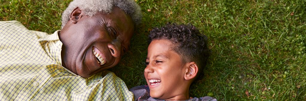 A grandfather and grandchild play in the grass.