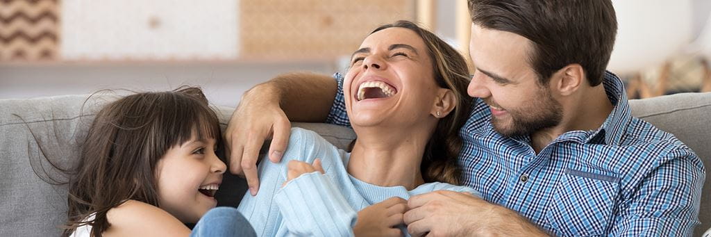 A cheerful family on living room couch tickling each other and laughing happily.