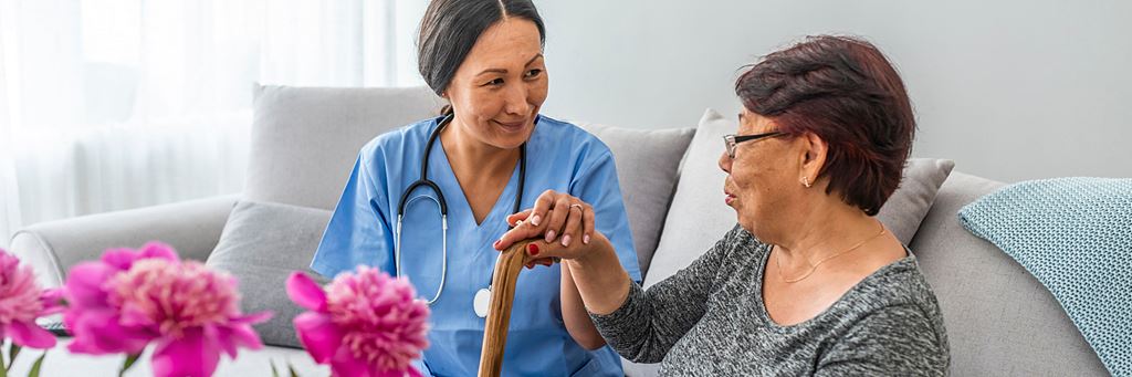 A nurse talks to a senior retiree in an assisted living facility while sitting on a couch.