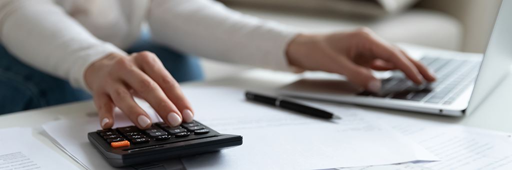 A person doing their taxes with a calculator, laptop, papers and pen.