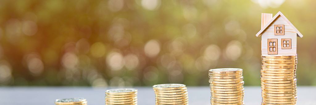 A tiny house balancing on a stack of coins with a grassy background.