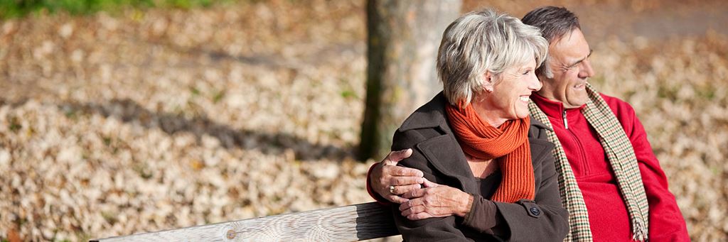An older couple sits on a bench outside.