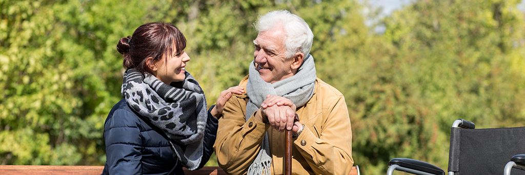 A senior man and his daughter sit on a park bench.