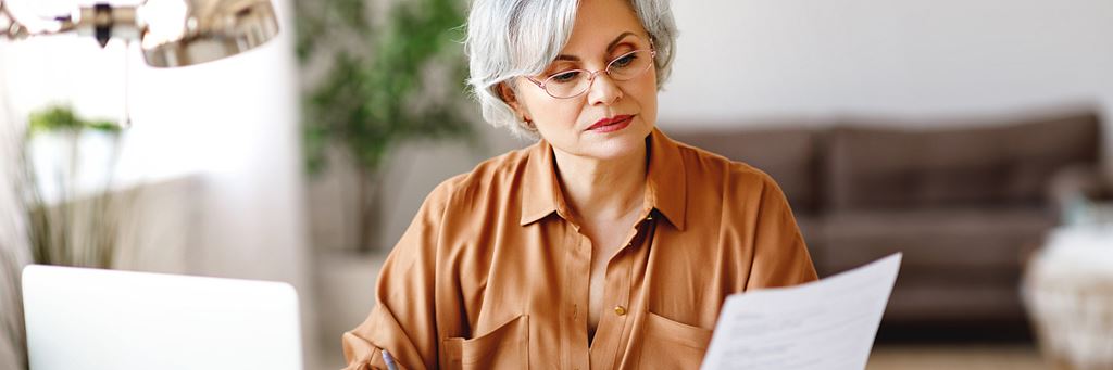 Woman seated at her desk with a laptop, taking notes with a pen.