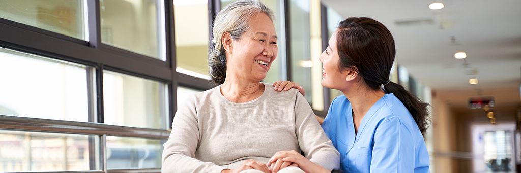 A respite caregiver talks with a smiling senior woman in a wheelchair.