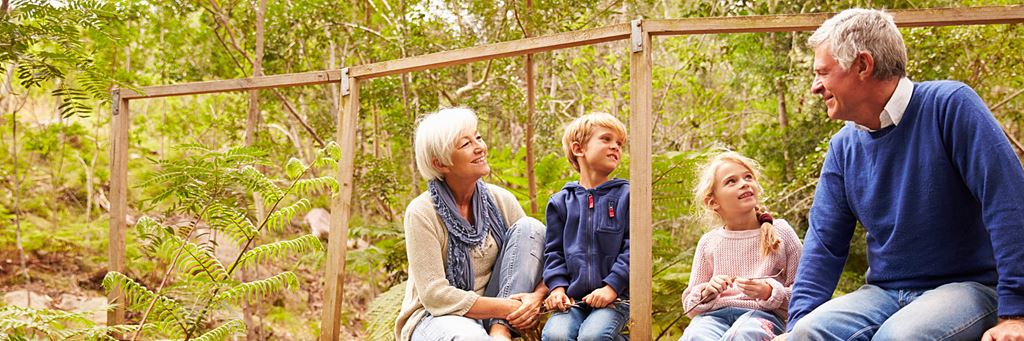 Two smiling grandparents sit outdoors with their grandchildren.