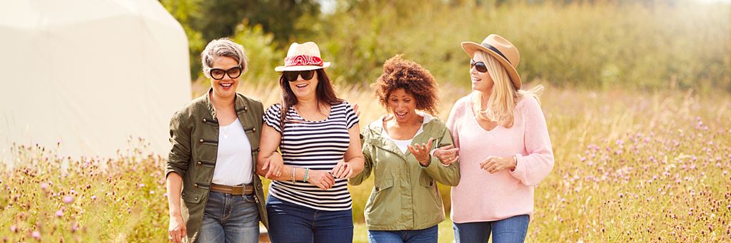 Four happy adult women walk together in a sunny field.