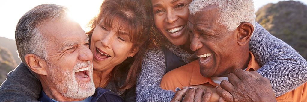 A group of four seniors smile and hug.