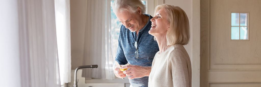 A senior couple laughs while preparing a meal in their home.