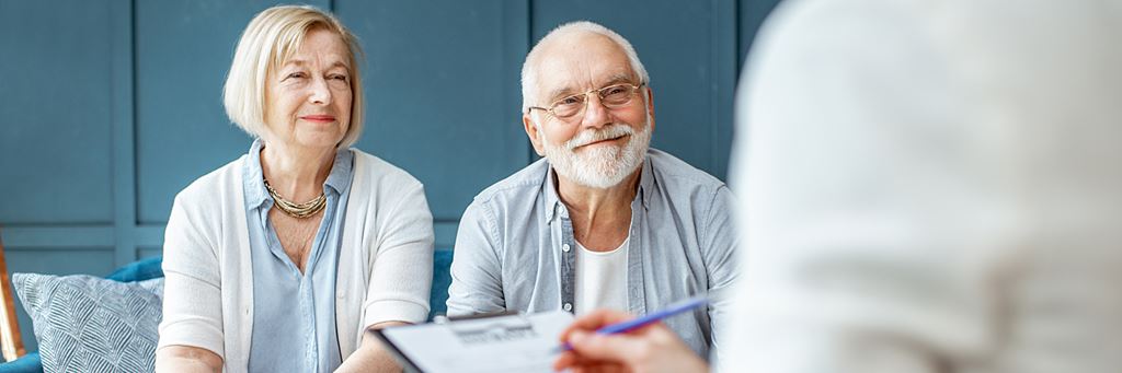 An older couple meeting with a retirement financial advisor who's writing an agreement on clipboard.