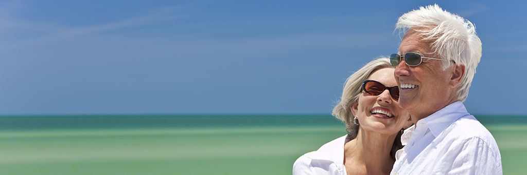 A senior couple smiling in front of the ocean.