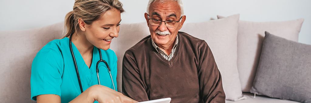 An elder care consultant shows her senior patient something on a tablet.