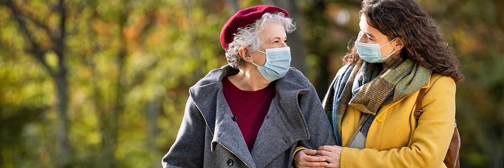 A middle-aged woman walks outdoors with an aging parent.