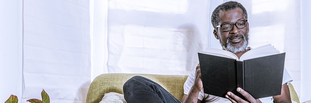 A man reading a book sitting on a couch.