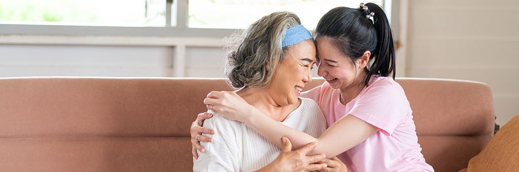 A senior mother and adult daughter hug.