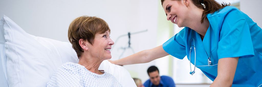 A patient in a bed sitting up while attended by a nurse.