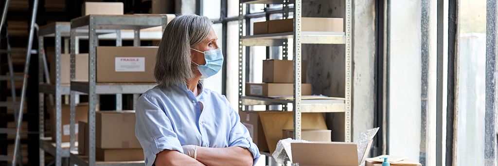 A woman business owner looks out the window in her company's stockroom.