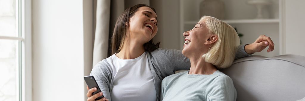 A retired mother and her adult child laugh while watching a video on a phone.