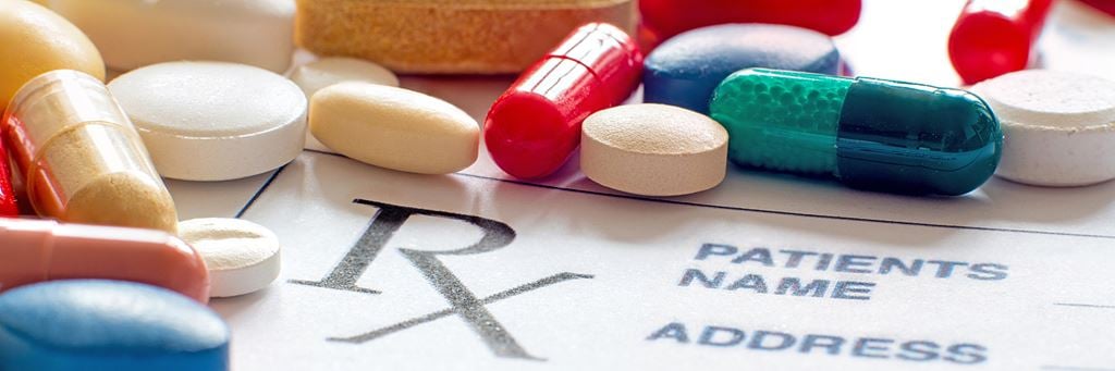 A pile of different pills on a prescription pad.