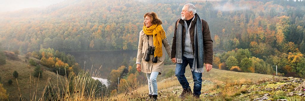 A retired couple walks together in a park.