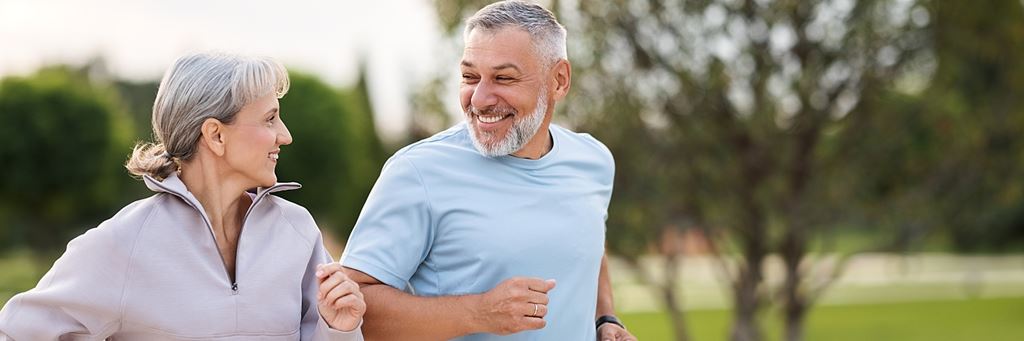 A smiling senior couple running outside.