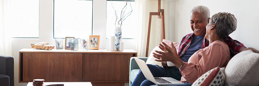 A senior couple sits on a couch with a laptop to discuss setting up a trust fund.