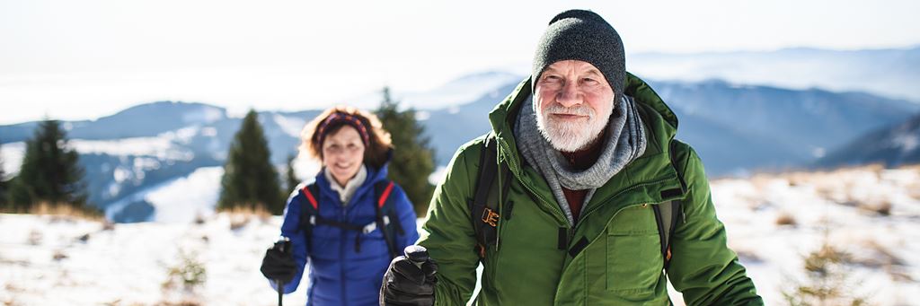 A couple wearing hats, gloves and warm coats snowshoes outside in the winter.