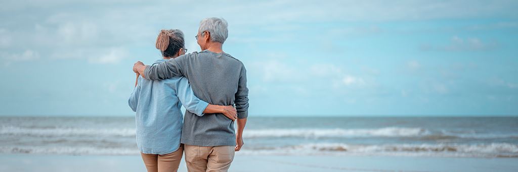 Two adults hug while walking next to each other on the beach.