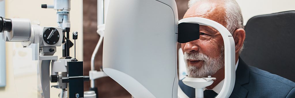 A senior man sits in front of an examination machine for an eye exam.
