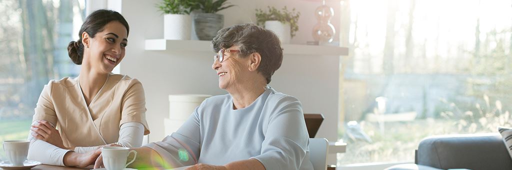 A senior woman and a caregiver laugh together while having tea.