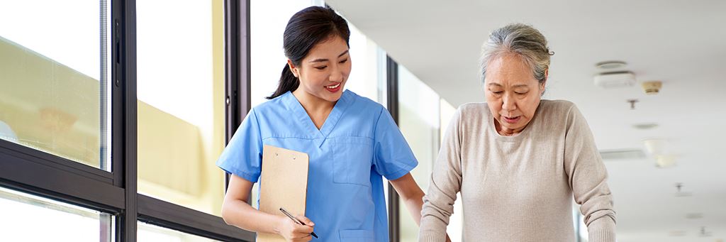 A senior woman walking with help from a health care professional.