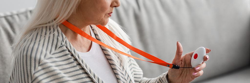 A senior woman examines a white medical alert pendant with a red emergency button.