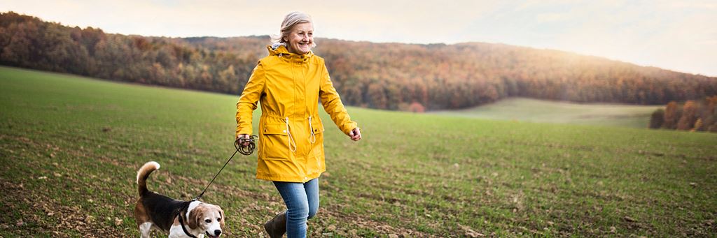 A senior woman walks her dog in a field.