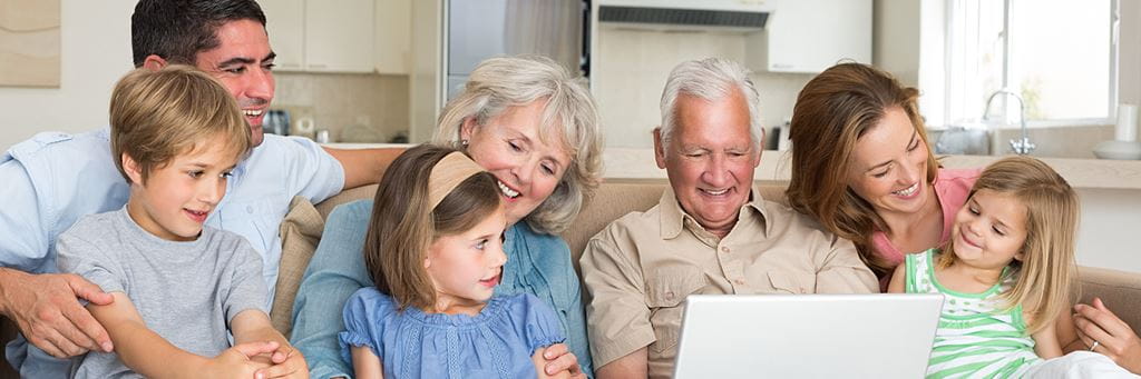 A multigenerational family sits together on the living room couch.