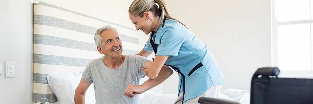 A nurse helps a senior man get out of bed in an assisted living facility.