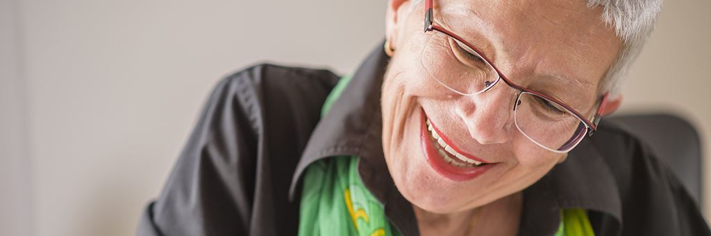 A smiling senior woman writes in a notebook.