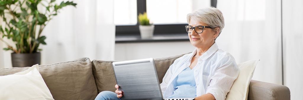 A woman researches high-deductible health plans on her laptop while sitting on a couch.