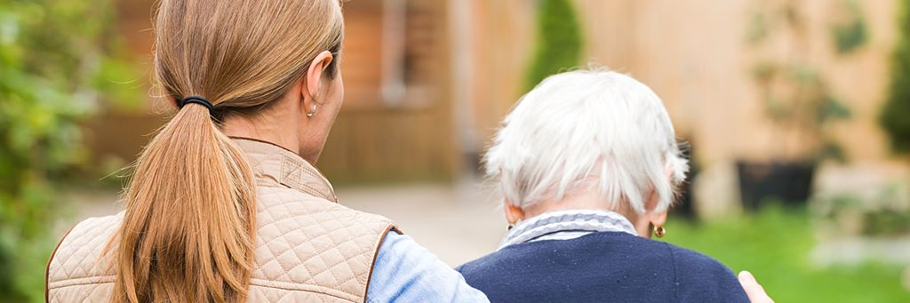 A caregiver helping a dementia patient walk outside.