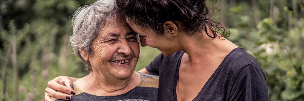 A woman and her older mother laugh together while walking outside.