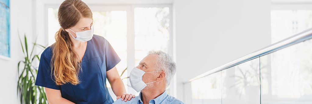 A medical professional wearing a mask talks to a senior patient wearing a mask.